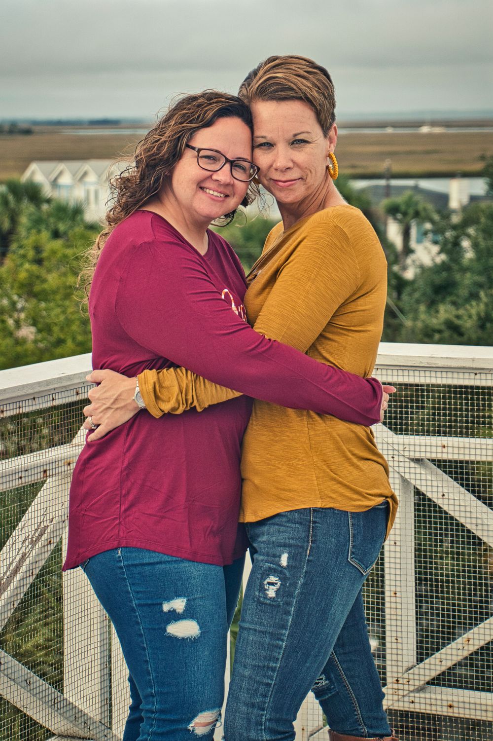 Two people embrace while standing on white observation deck overlooking coastal landscape.