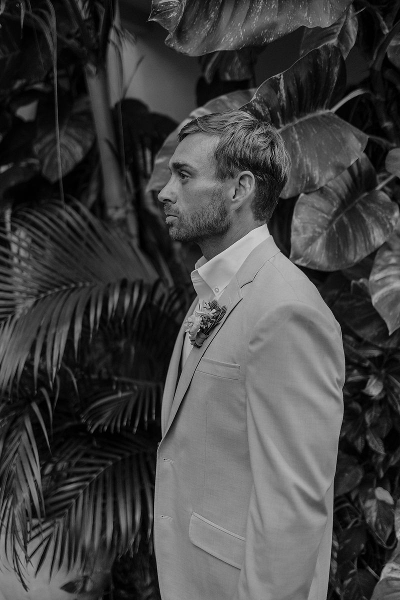 Black and white portrait of someone wearing a light suit surrounded by tropical foliage.