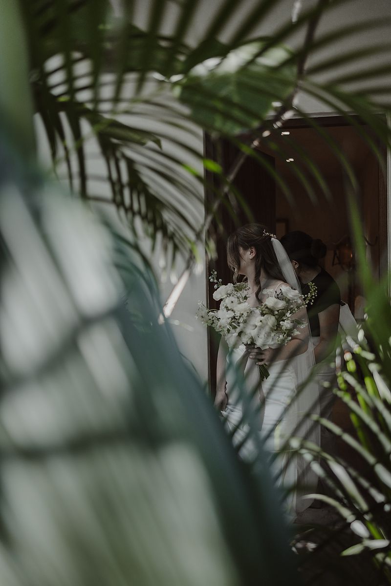 Artistic shot through leaves of bride in gown at La Valise Tulum elopement Riviera Maya wedding photographer.