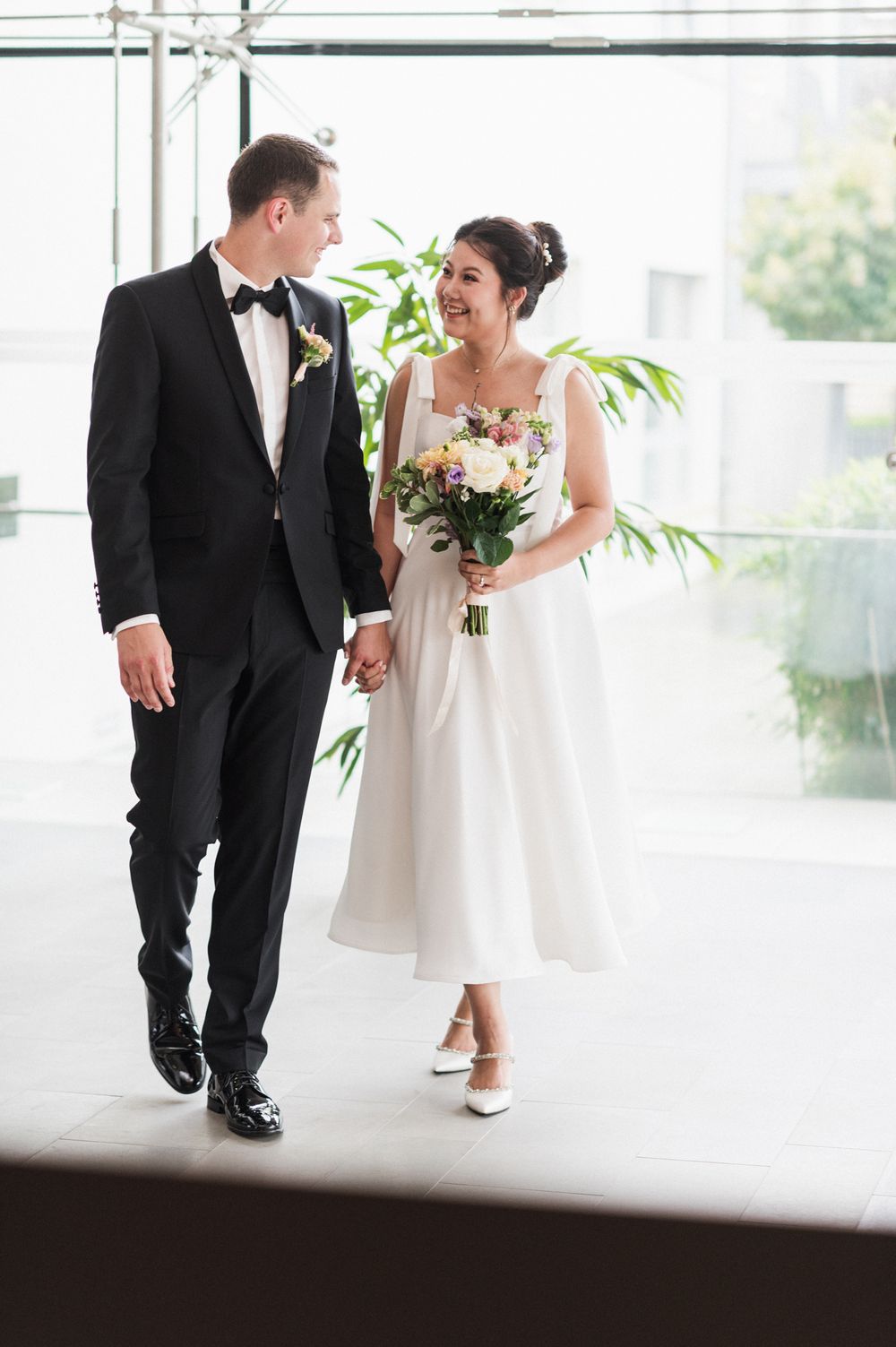 Newlyweds share a joyful moment while walking together in a bright hallway.