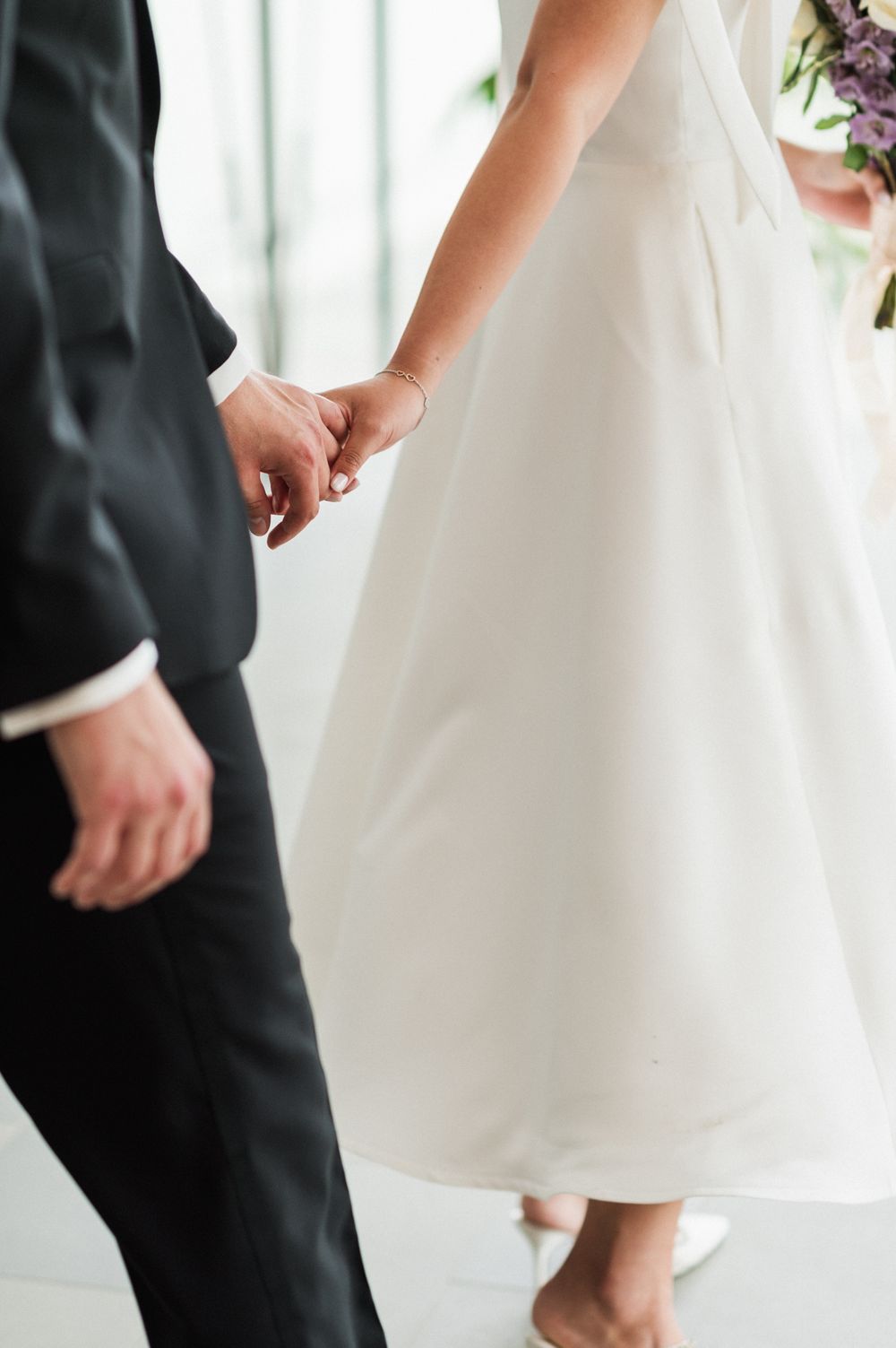 Close-up view of a couple holding hands, with the bride in a white dress and groom in a dark suit.