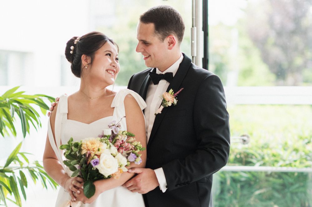 Newlyweds share tender moment in formal attire while holding colorful bridal bouquet.