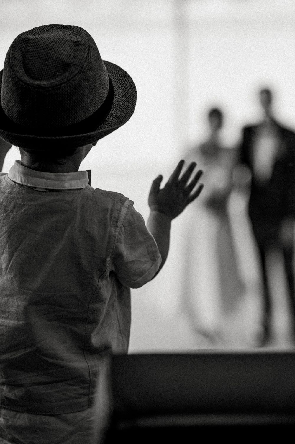 Young child in a black hat waves at a wedding couple in silhouette.