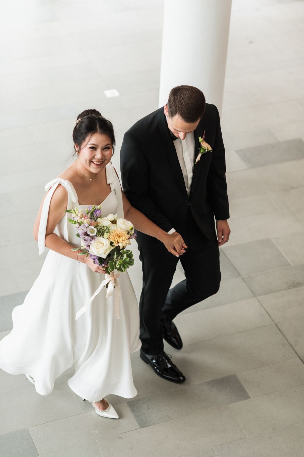 Wedding couple walking together in modern venue with white columns and geometric flooring.