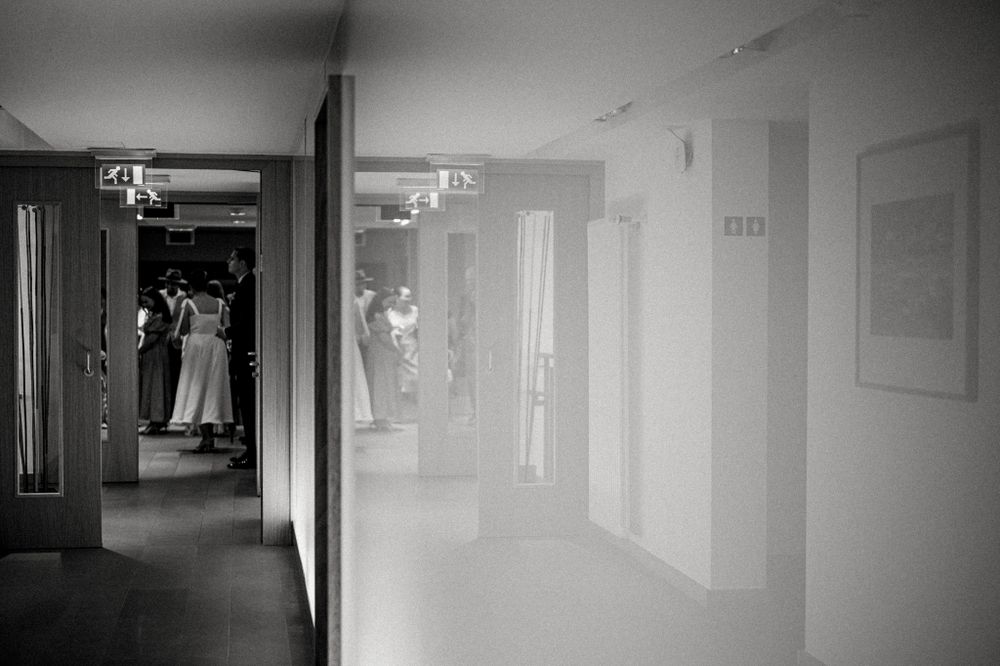 Black and white photograph of a long hallway with reflective floors and bright lights overhead.