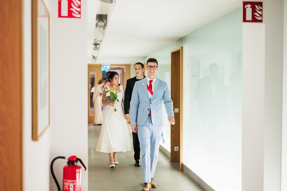 Couple walks down a modern hallway with white walls and red fire extinguisher signs.