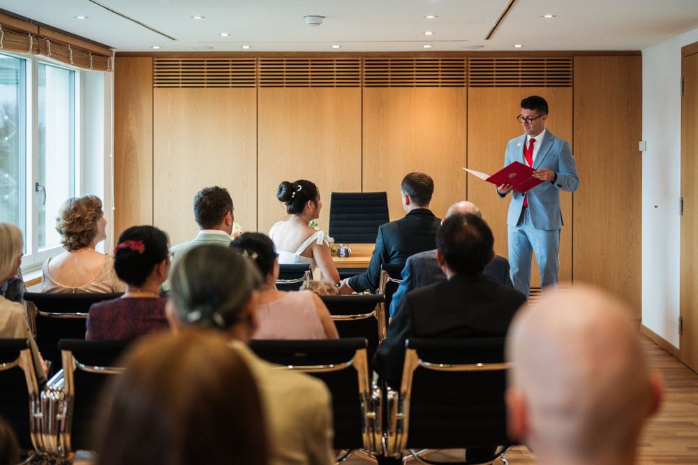 Wedding ceremony in modern wood-paneled room with guests seated in rows.