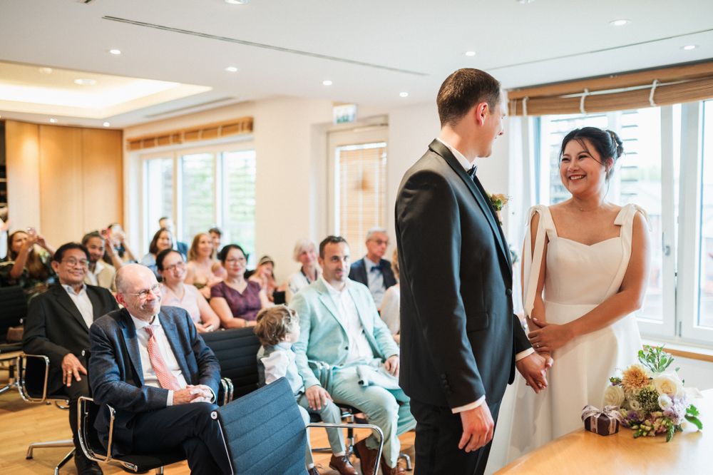 Wedding ceremony in progress in a modern room with large windows and seated guests.