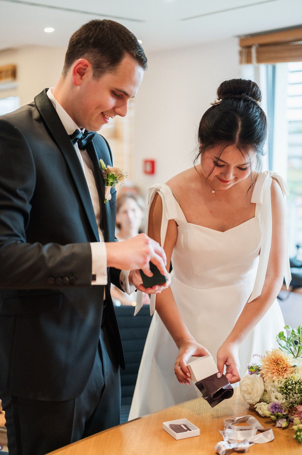 A couple at their wedding ceremony pouring drinks together in a light-filled room.
