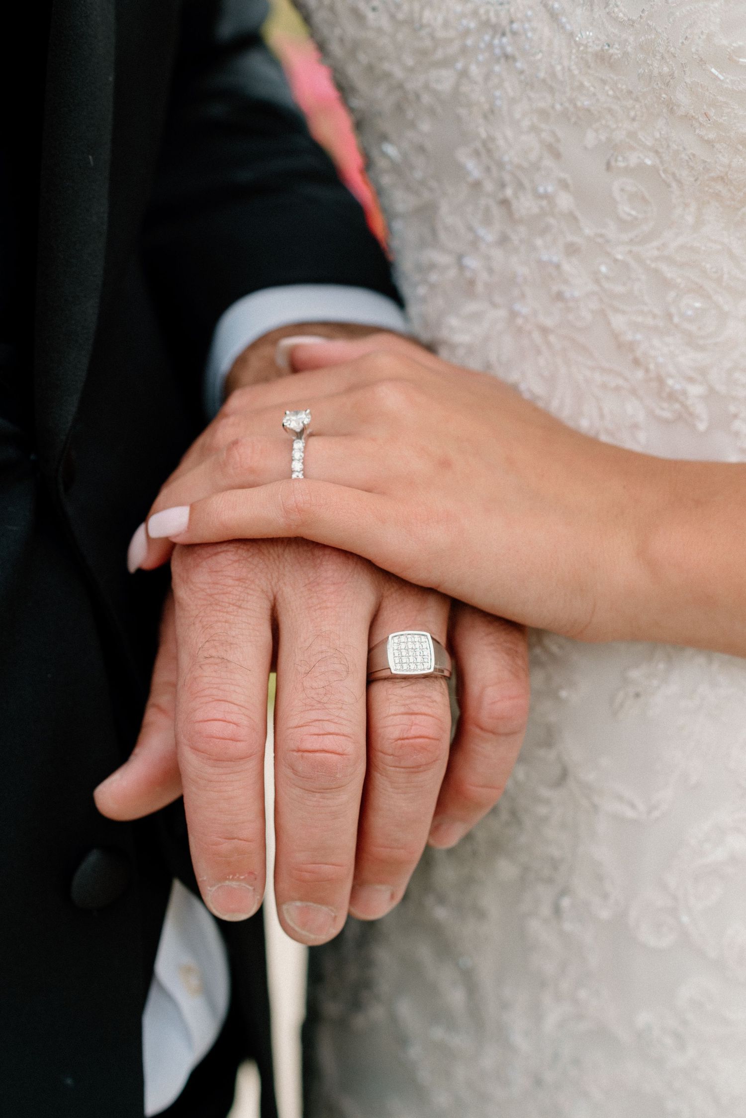 Close-up shots of wedding rings and clasped hands against white lace dress fabric.