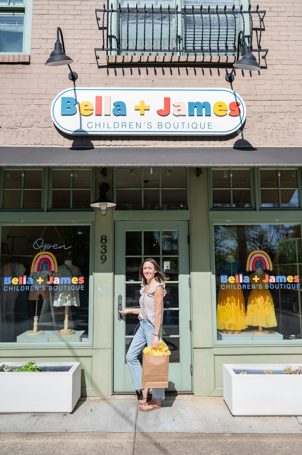 Exterior view of Bella + Luna children's boutique storefront with rainbow window displays and signature signage.