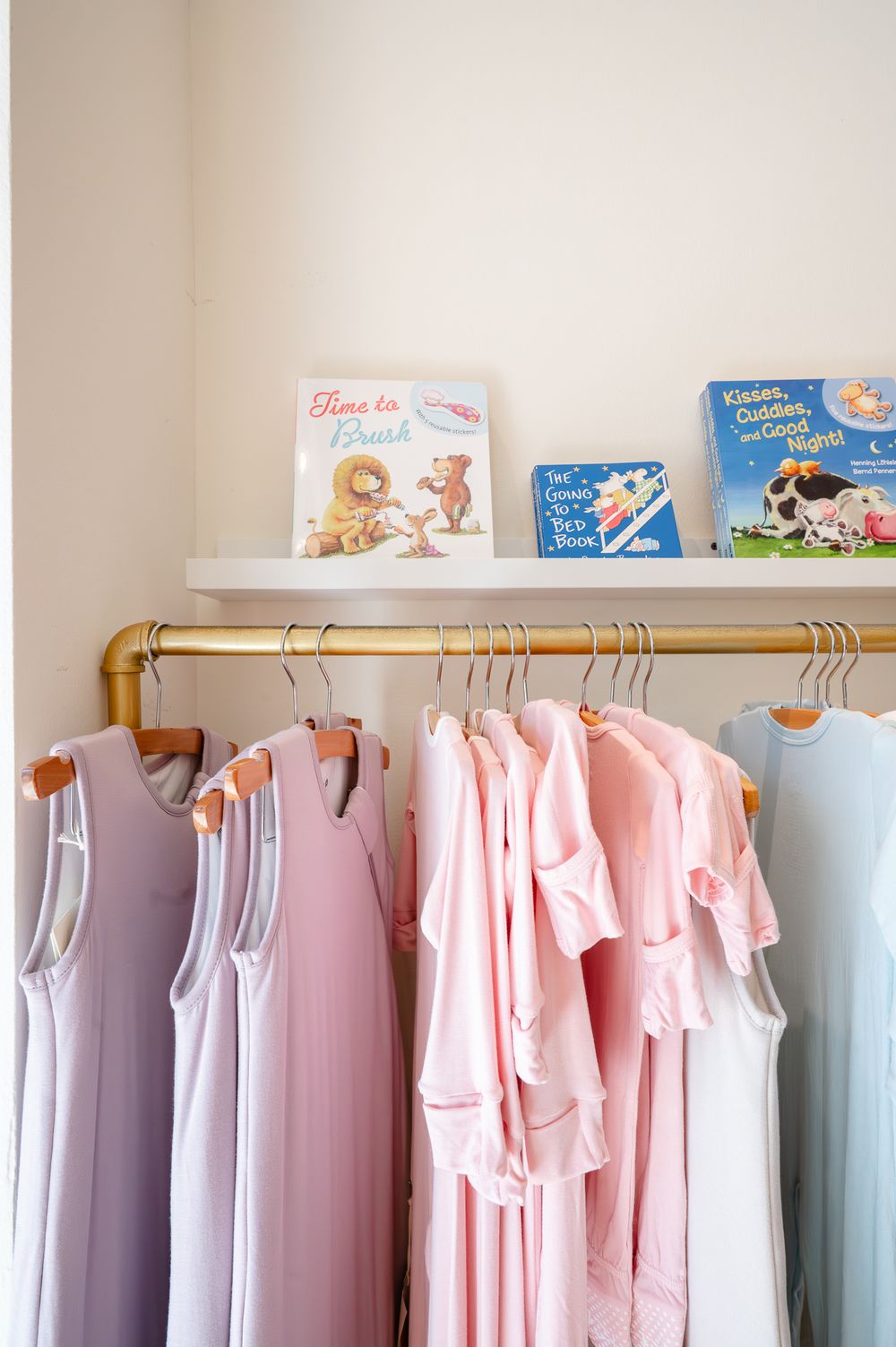 Pastel colored bridesmaid dresses hanging on a gold clothing rack with children's books displayed on shelf above.