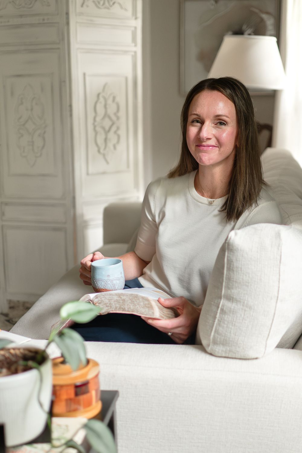 Cozy reading scene with blue mug and book on white couch.