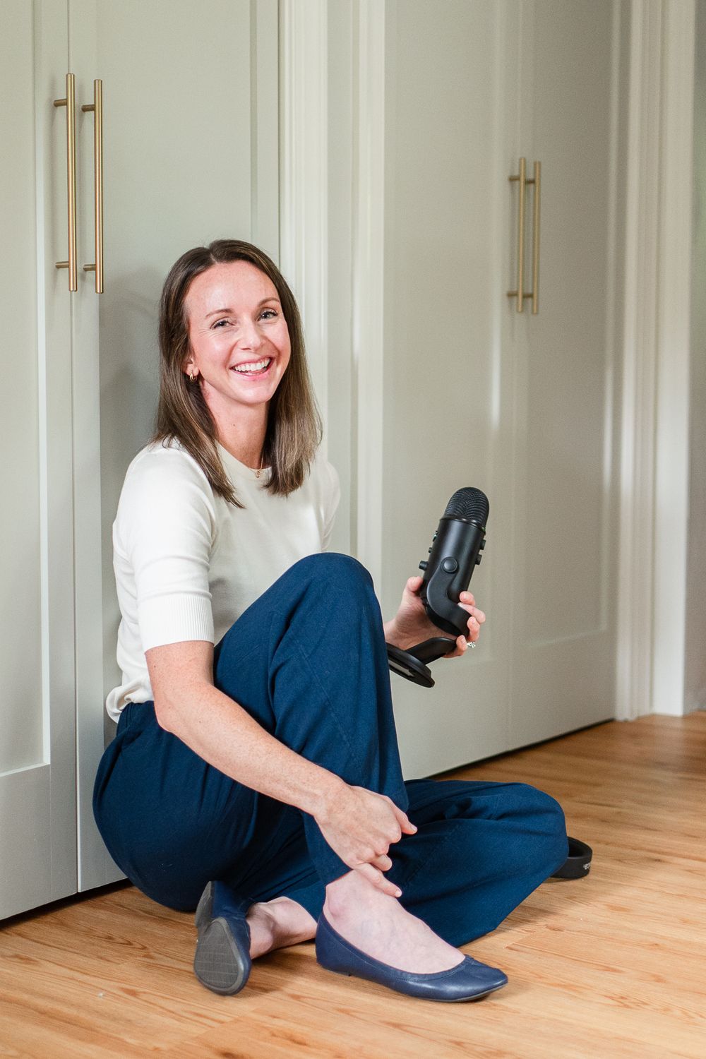 Casual home setting with person sitting on floor holding phone by white cabinets.