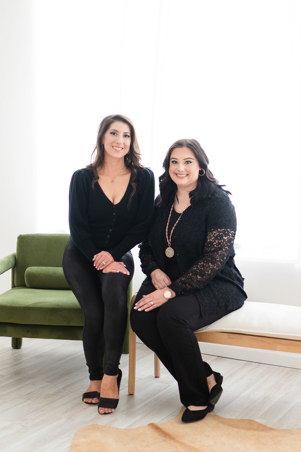 Two women in black outfits sitting together on modern furniture in bright room.