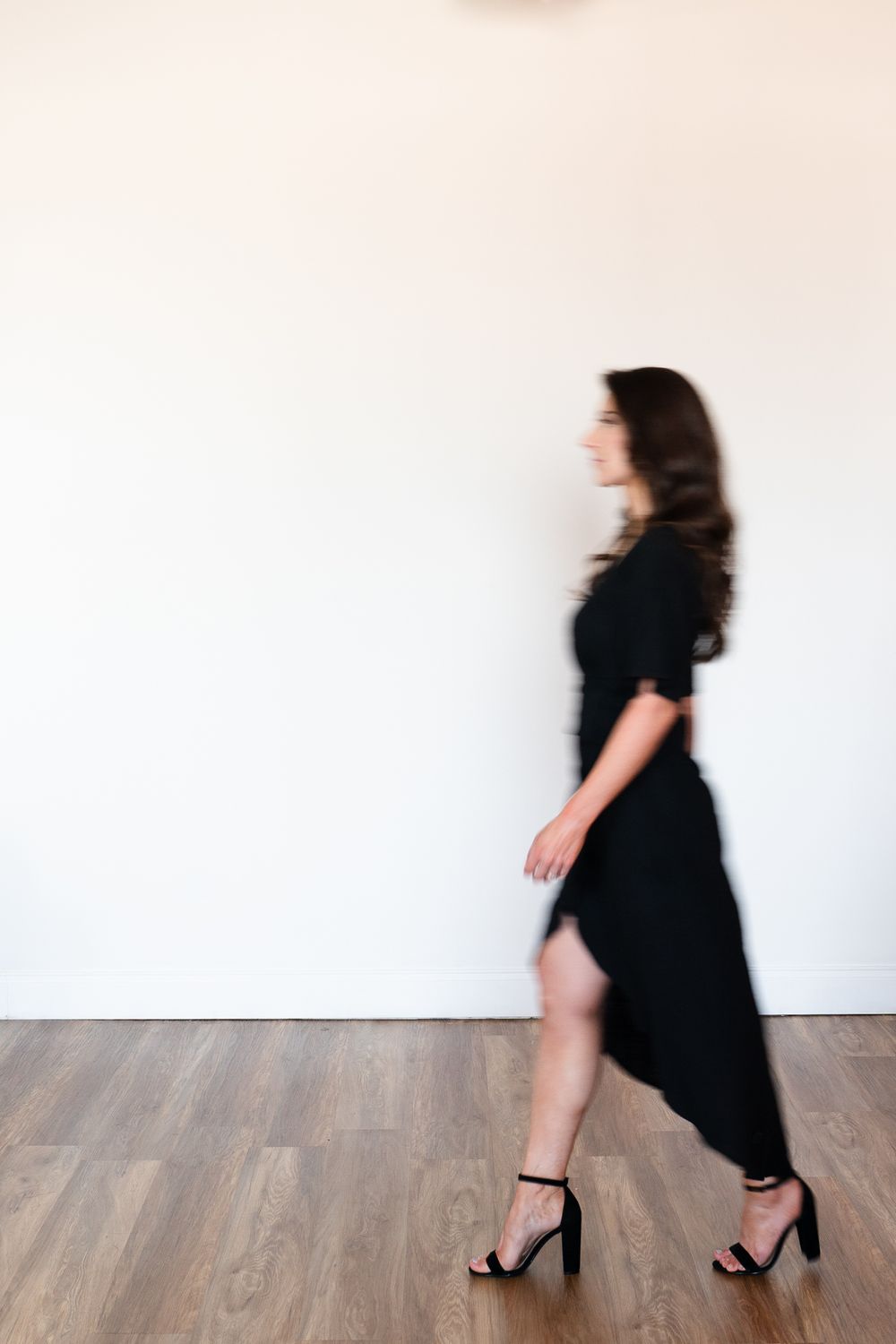 Motion blur photo of person in black dress walking across wooden floor.