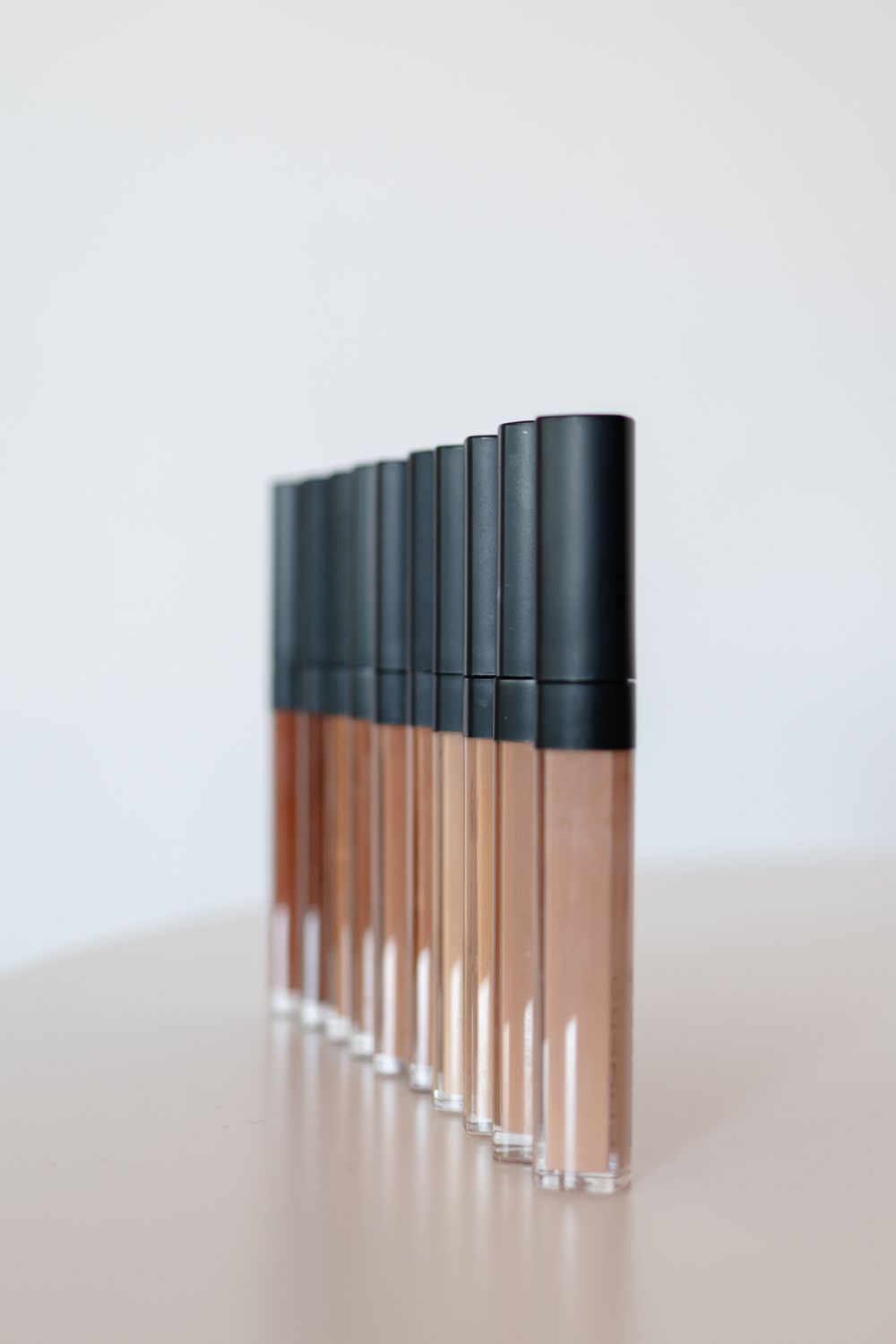 A row of makeup concealer tubes arranged in gradient colors from light to dark against white background.
