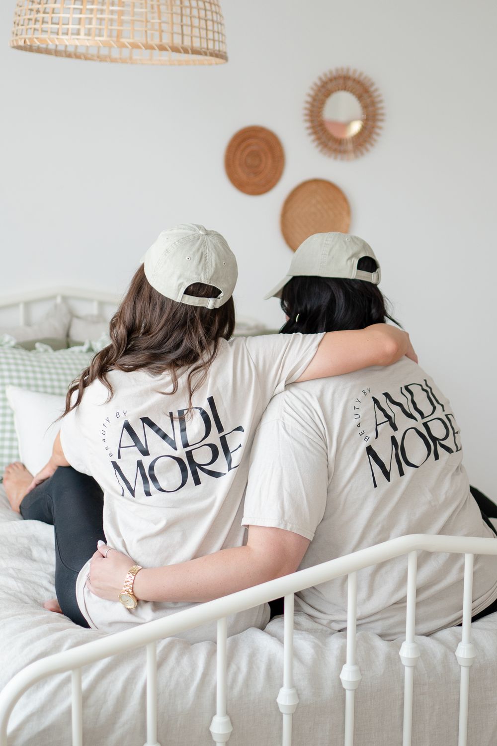 Two people wearing matching white 'AND MORE' t-shirts and baseball caps sitting together on a bed.