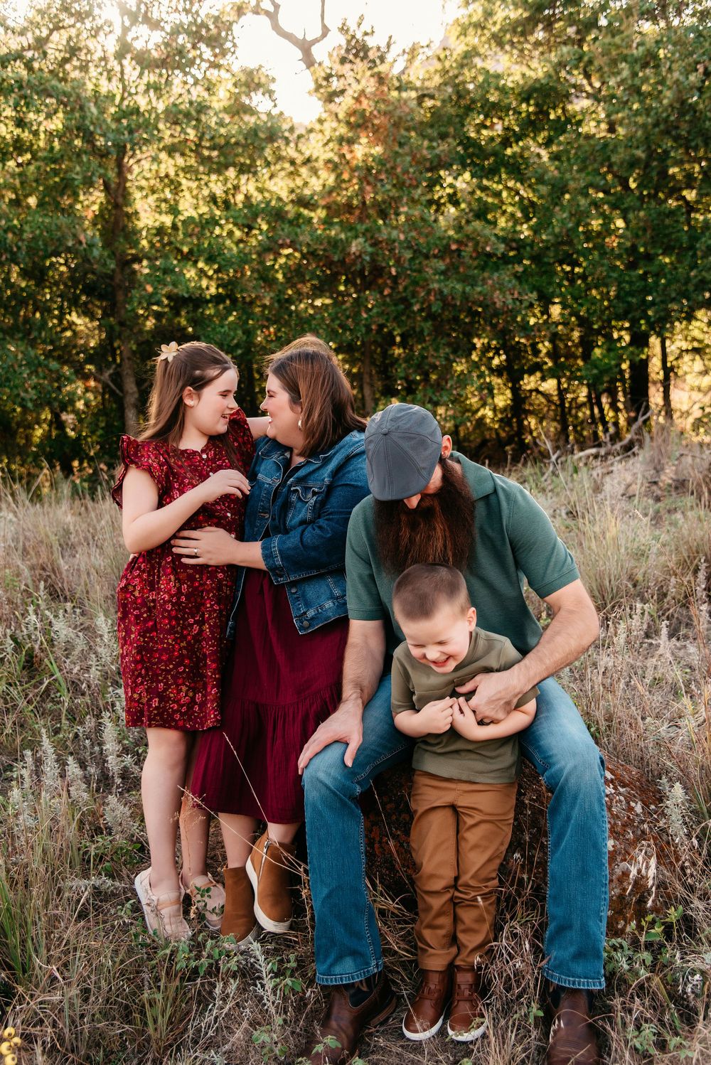 A family shares tender moments together in a field during golden hour sunset.