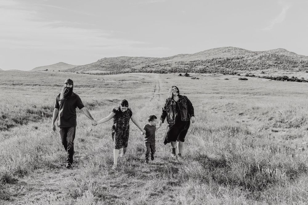 Black and white landscape photo of people walking through a grassy field with mountains in background.