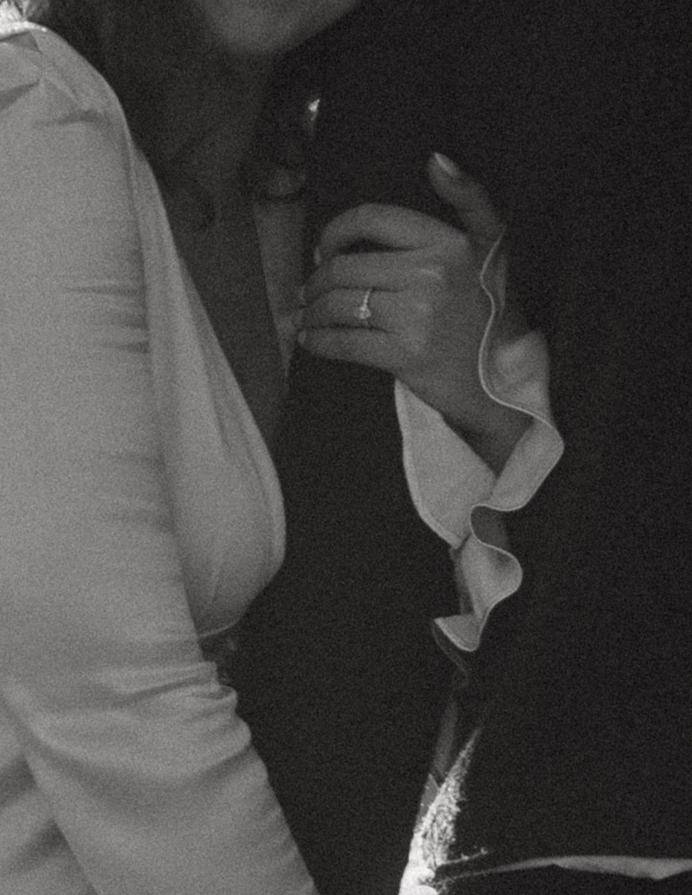 Close-up detail shot of couple's hands and formal attire in black and white.