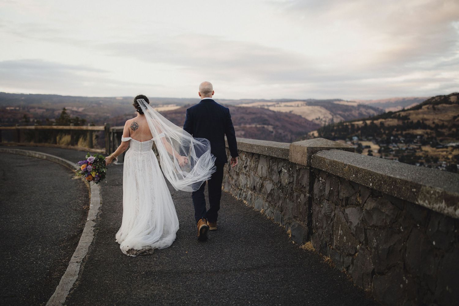 Bride and groom kissing on a terrace with a stunning lake and mountain backdrop, bride holding a colorful bouquet.