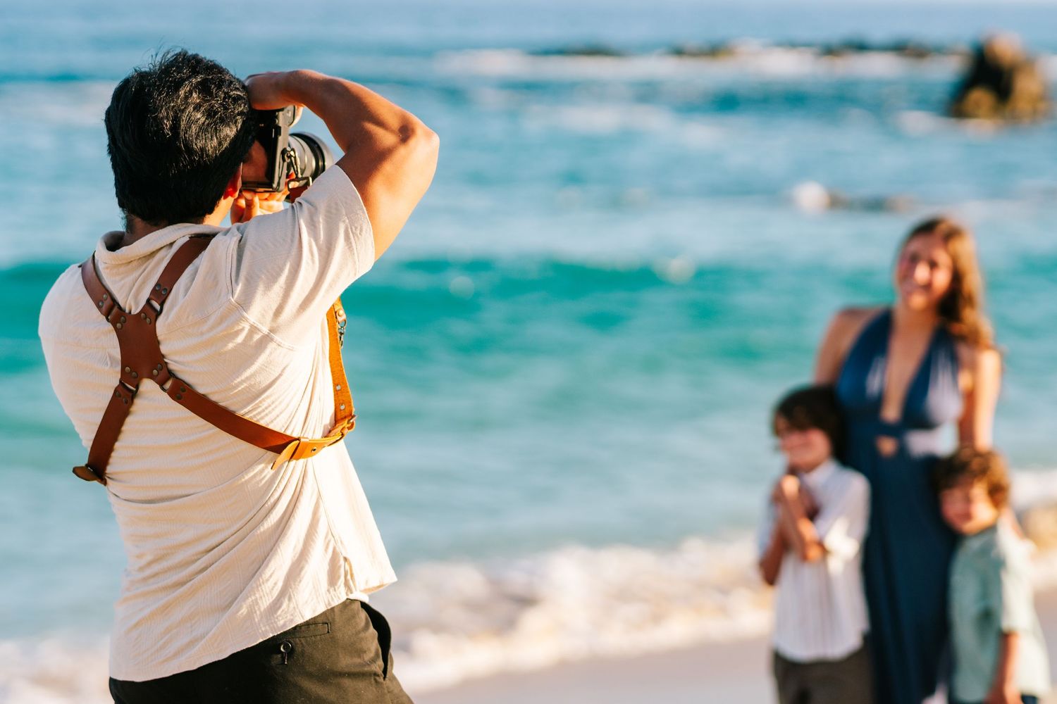 Photographer capturing a family portrait on a sunny beach with turquoise ocean waves in the background.