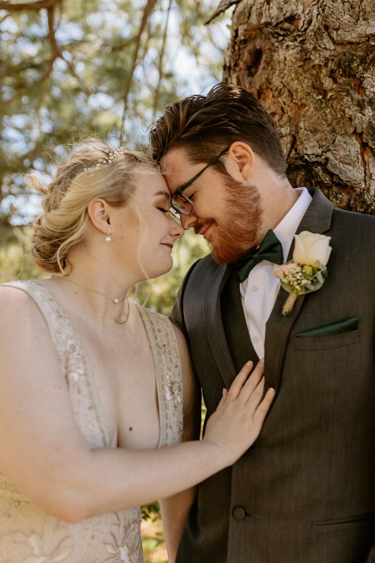 Bride and groom share a romantic forehead-to-forehead moment outdoors, with the groom wearing a gray suit and boutonniere at Lake Cuyamaca.