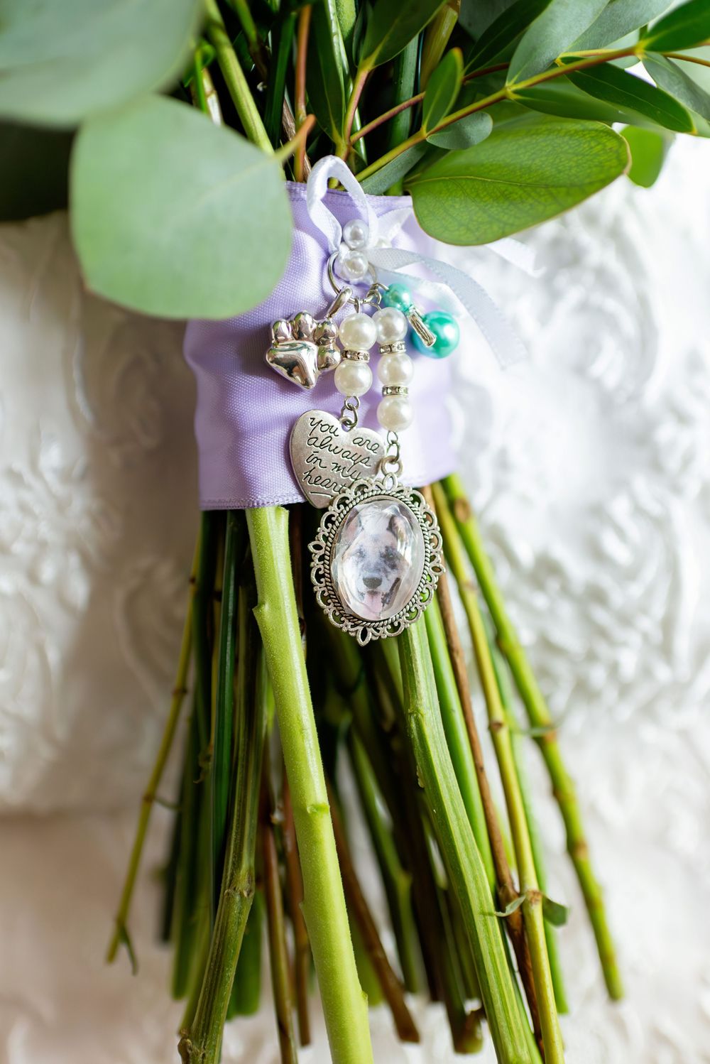 Silver locket and pearl charms tied with lavender ribbon to a bridal bouquet with eucalyptus greenery.