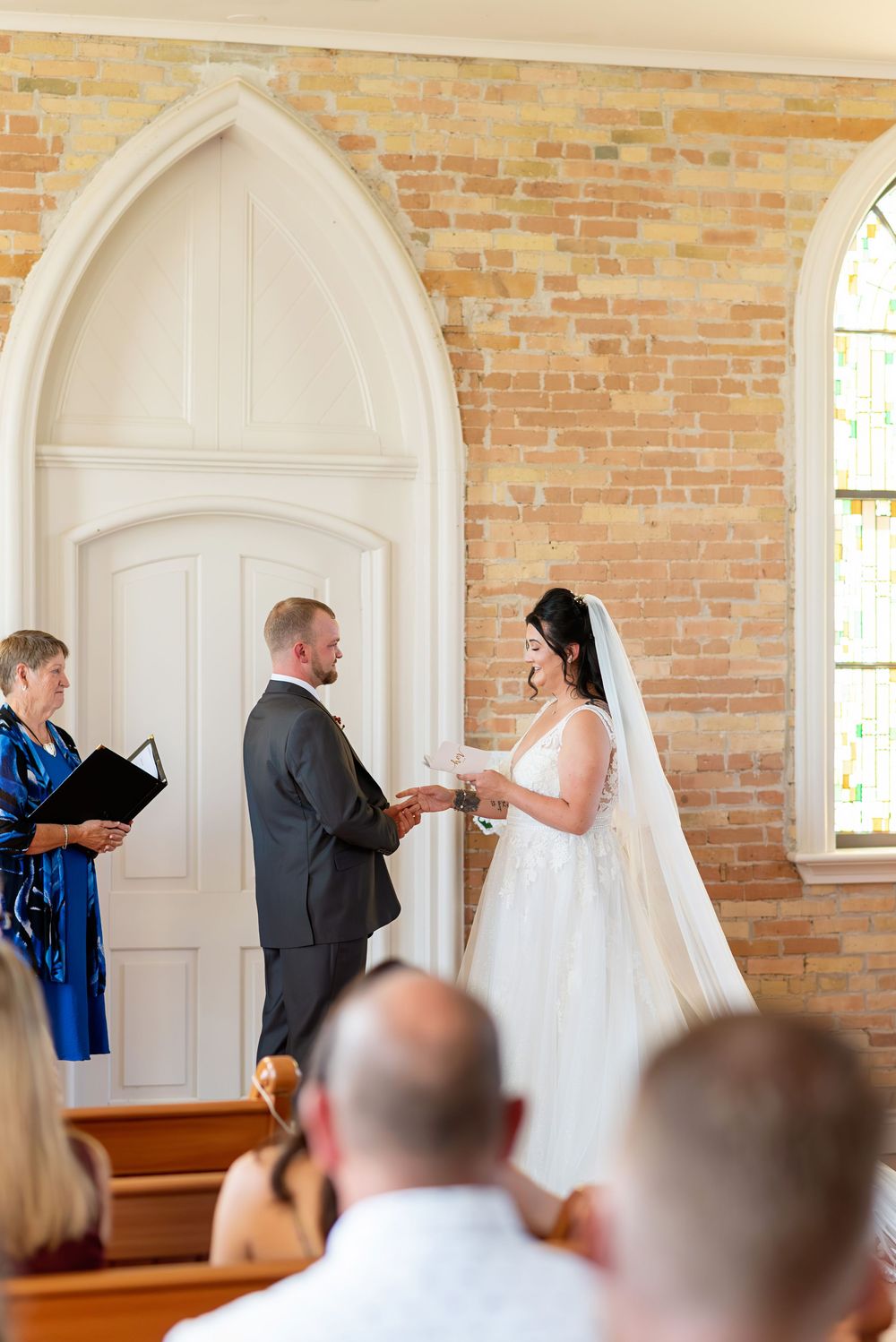 Bride and groom exchange vows at a charming chapel wedding ceremony with exposed brick walls and arched windows.