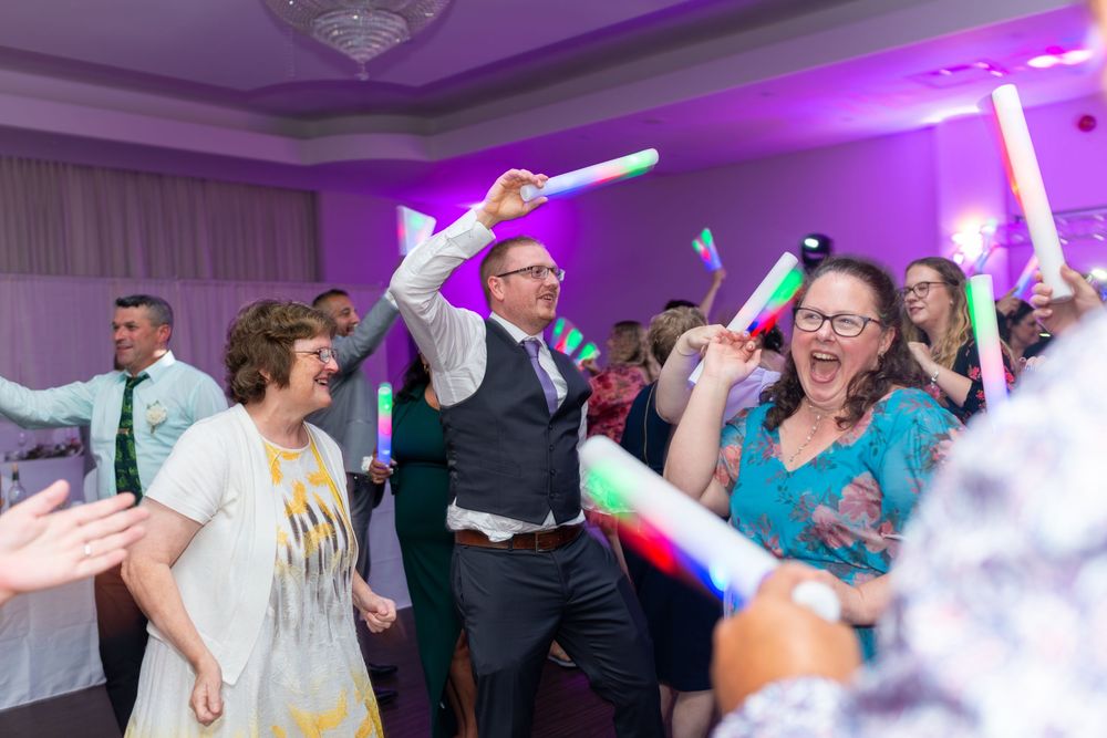 Guests dancing and celebrating with colorful glow sticks at a lively wedding reception party.