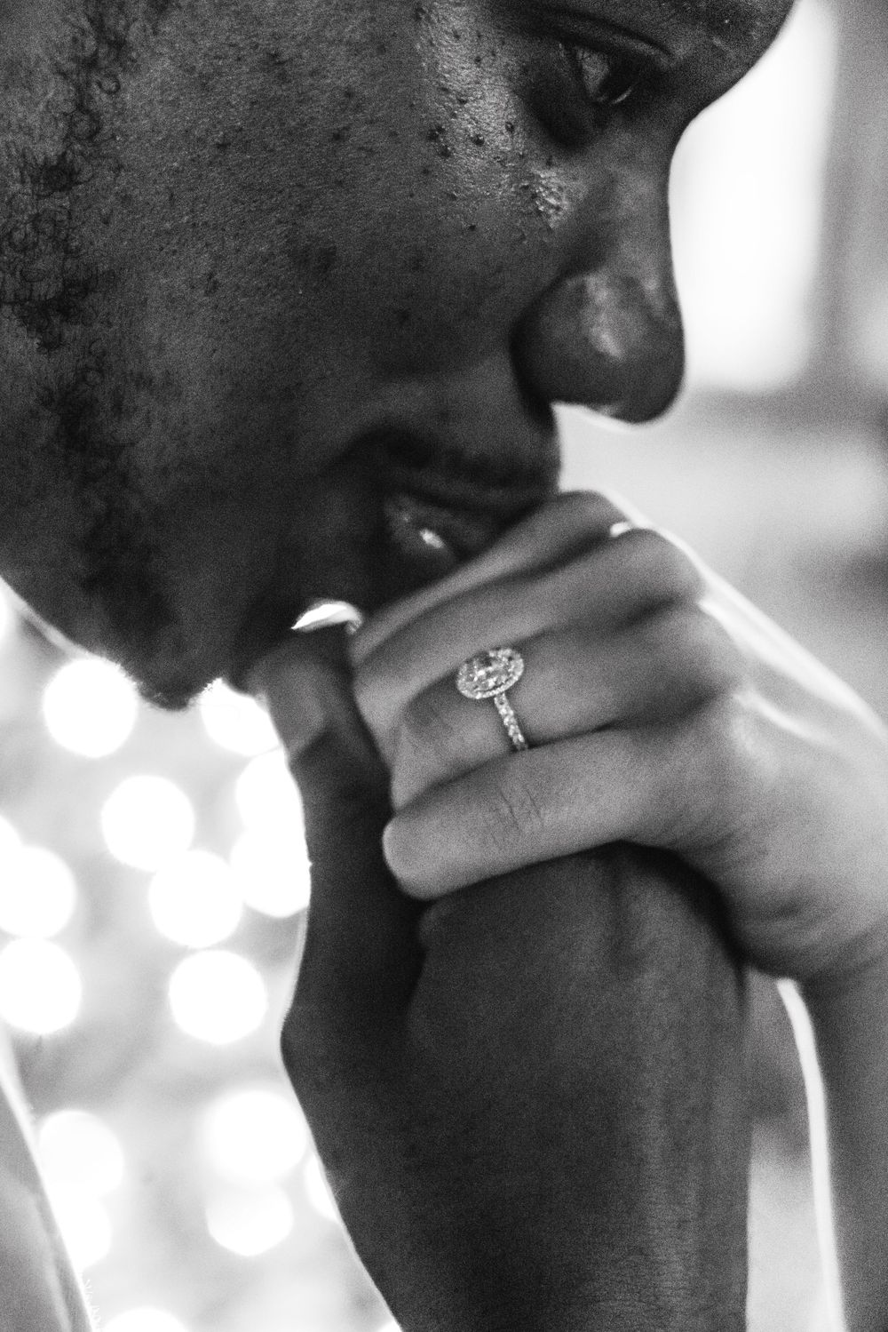 Black and white photo of a man admiring a diamond halo engagement ring on a woman's hand.