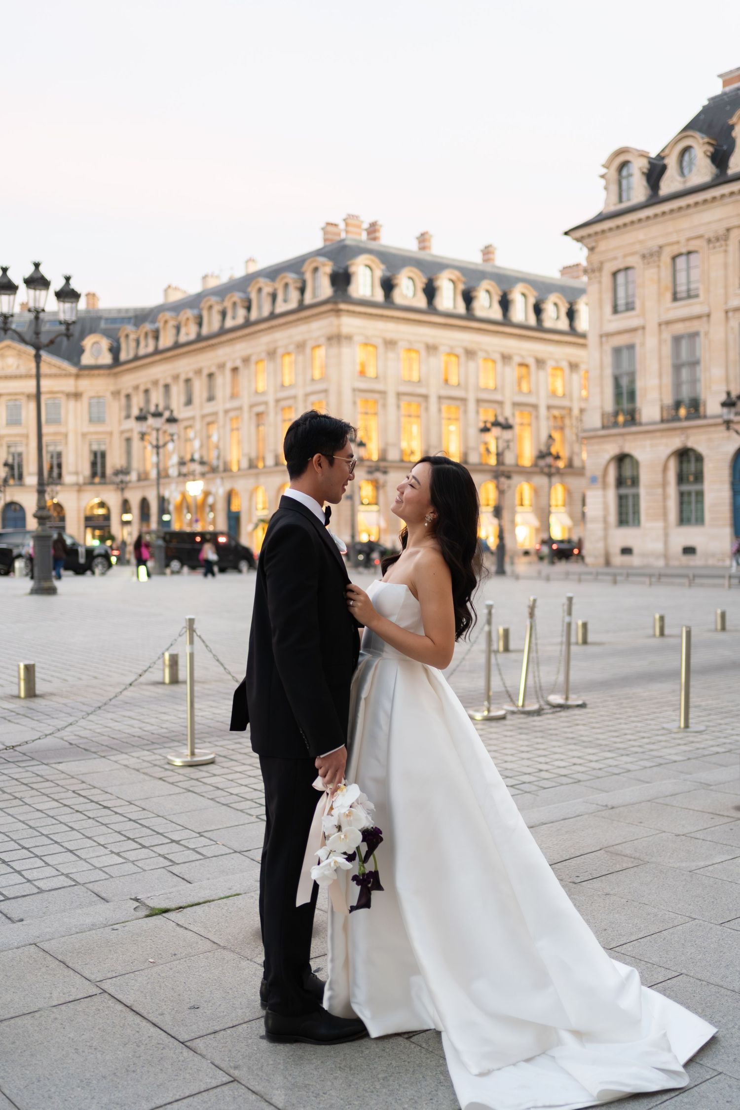 Bride and groom share a romantic moment at Place Vendôme in Paris, with elegant Haussmann buildings glowing at dusk.