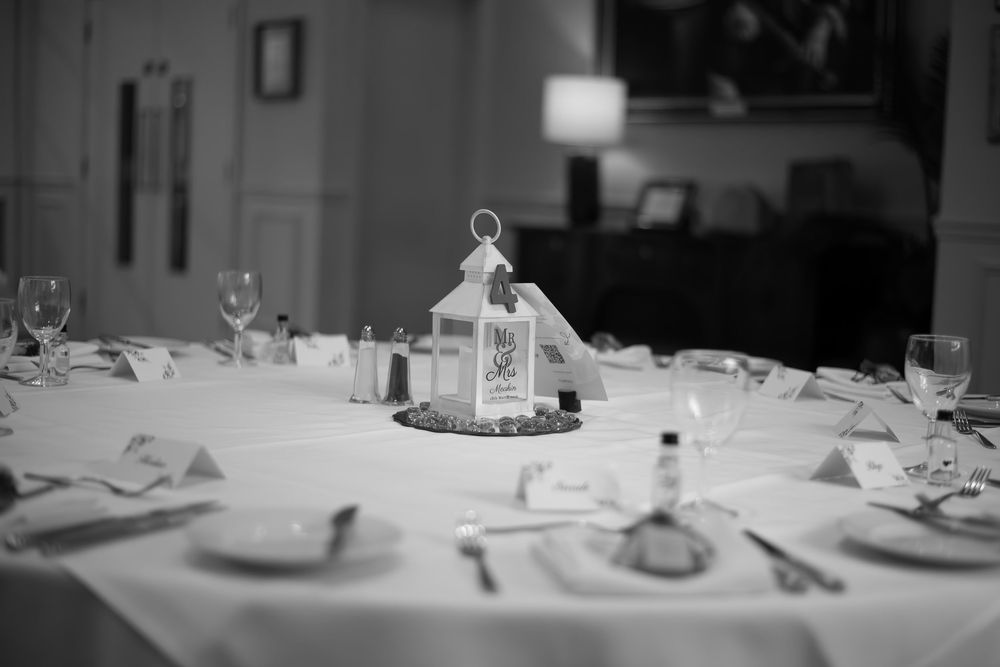 Black and white photo of an elegant wedding reception table set with glassware, cutlery, and a lantern centerpiece.