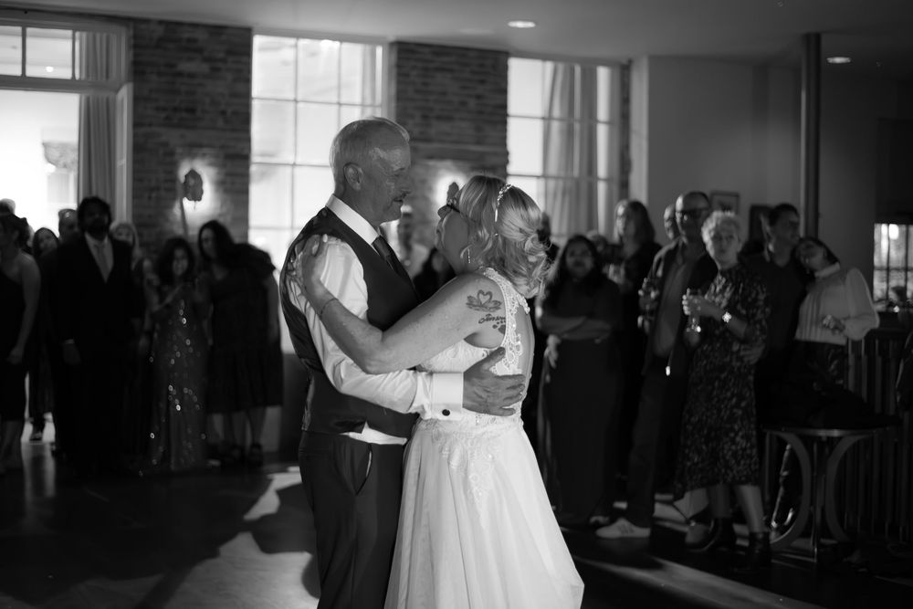 Black and white photo of a bride and older man sharing an emotional father-daughter dance at a wedding reception.