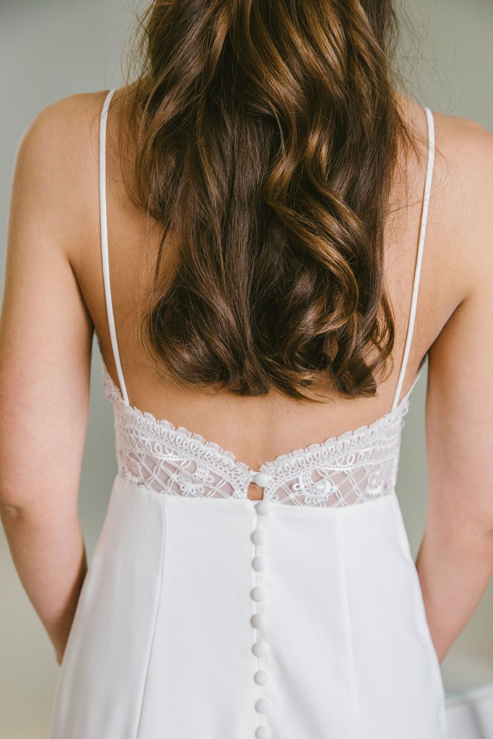 Bride in white lace spaghetti strap wedding dress with button back detail and flowing brunette hair.