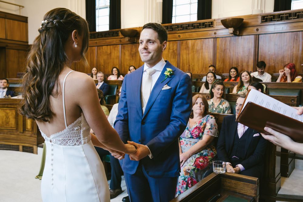 Groom in blue suit holds brides hands at altar during wedding ceremony in elegant venue.