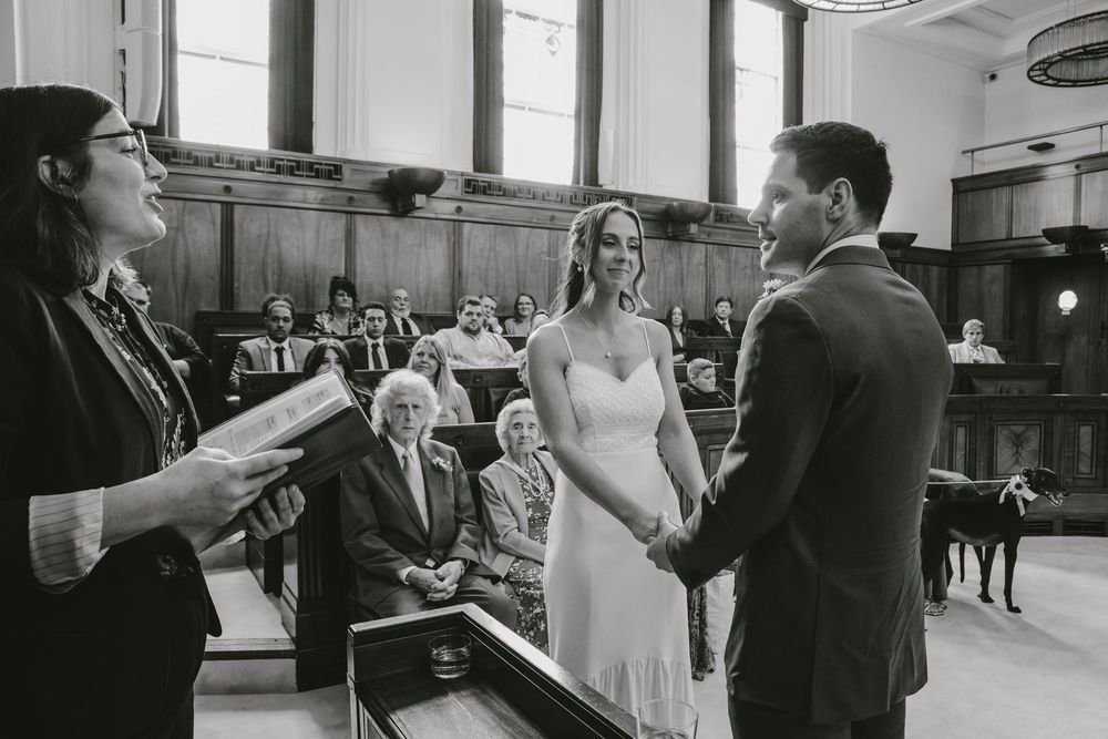 Black and white photo of couple exchanging vows before officiant at intimate wedding ceremony.