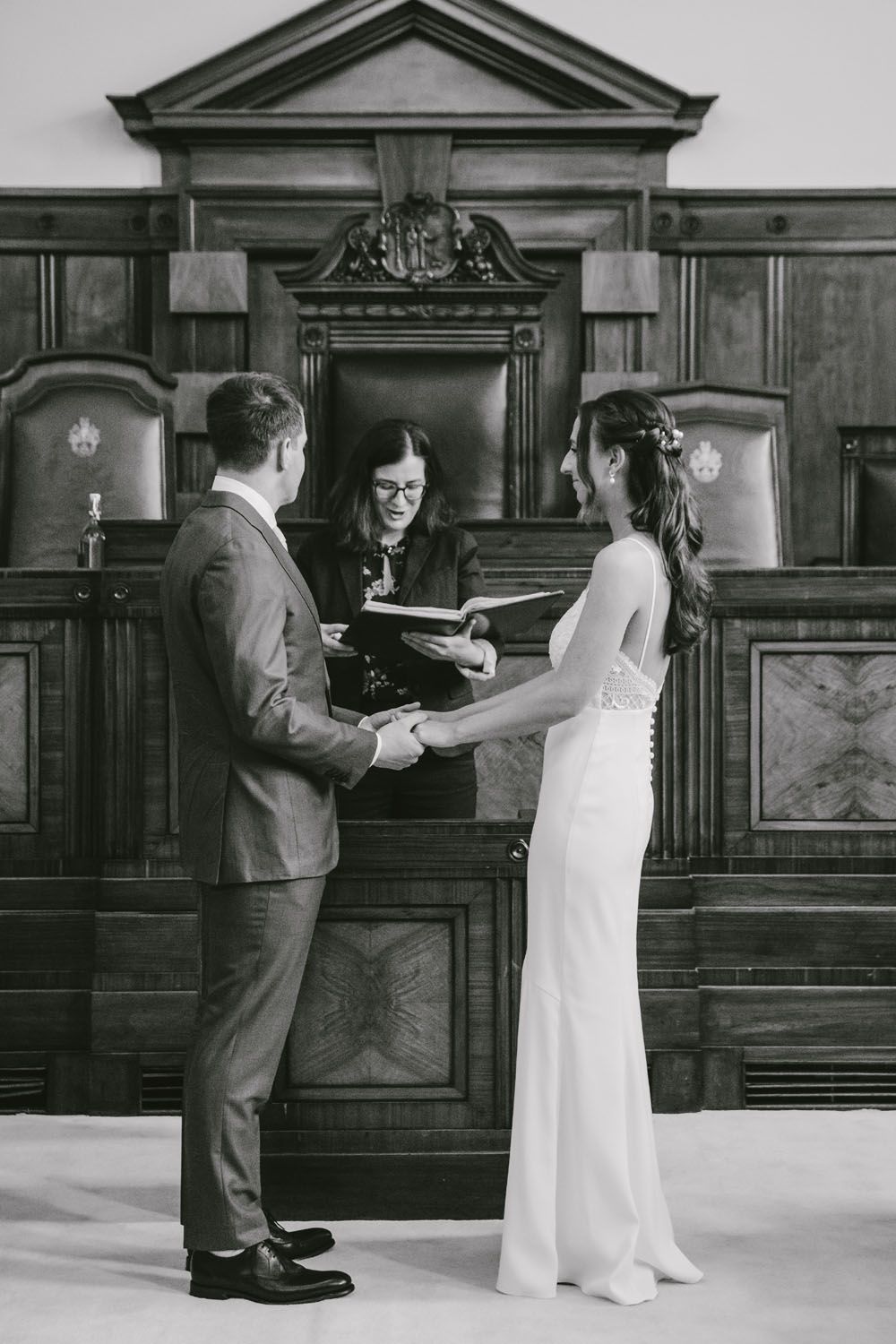 Black and white photo of a couple exchanging vows at a courthouse wedding ceremony with an officiant holding a book.