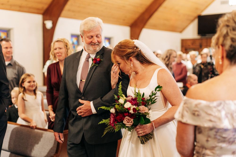 Emotional bride walking down the aisle with her father at a church wedding ceremony, holding a bouquet.