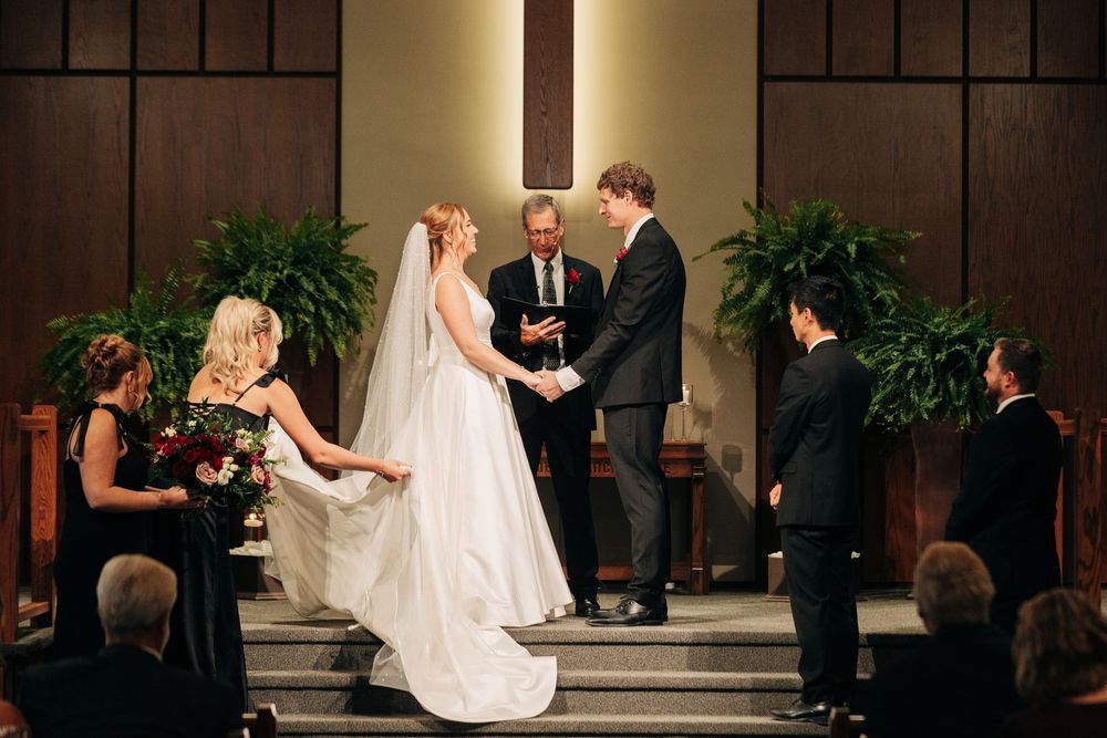 Bride and groom exchange vows at a church altar with wedding party and officiant present.
