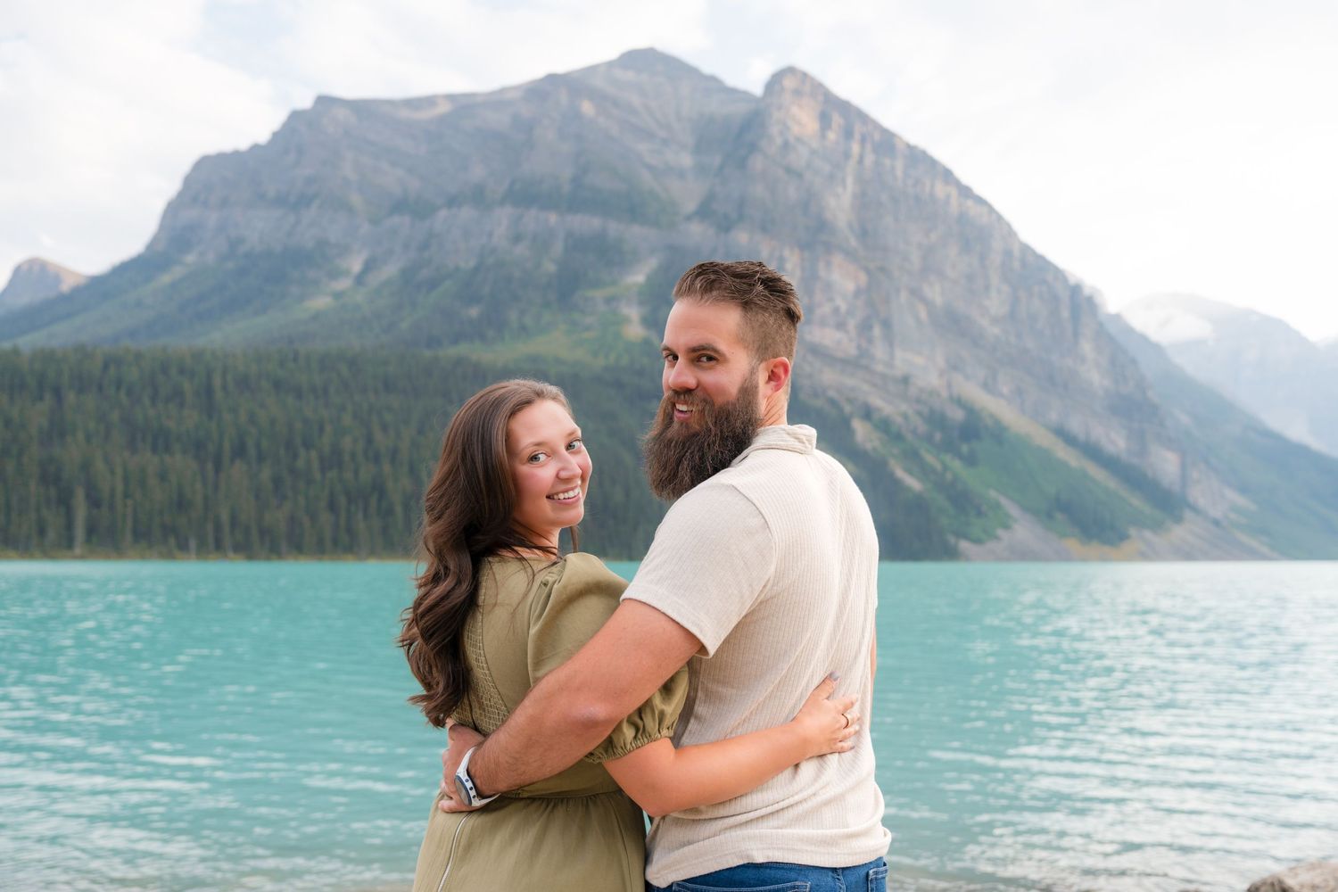 Couple embracing and smiling at turquoise Lake Louise with stunning mountain backdrop in Banff National Park.