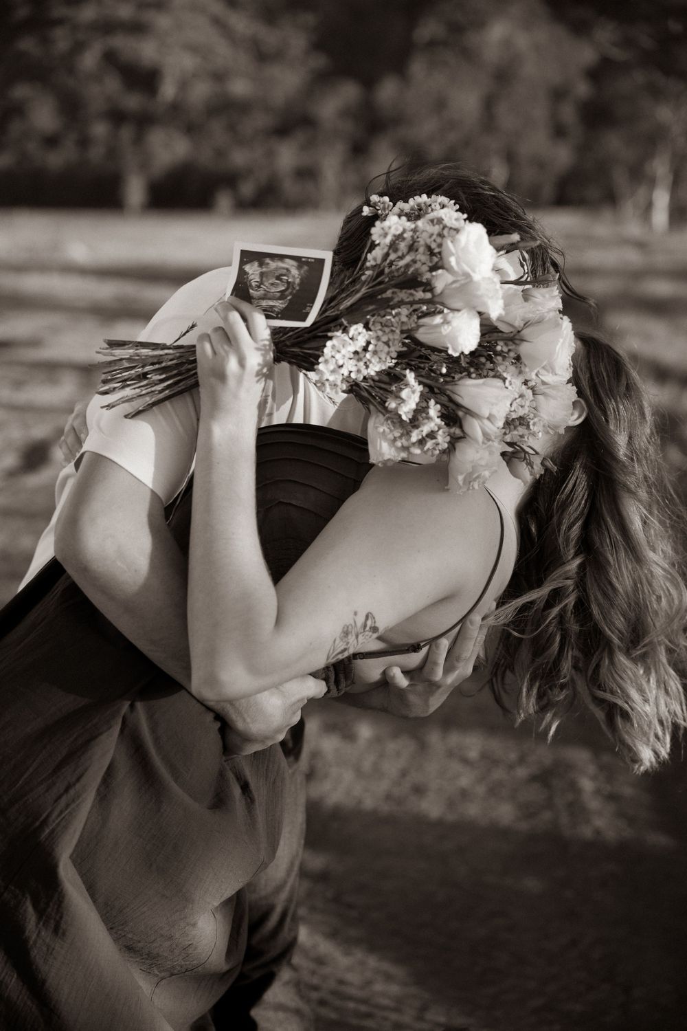 Couple embracing holding ultrasound scan and flower bouquet, sepia tone pregnancy announcement photo. maternity photo. Rockhampton queenslan