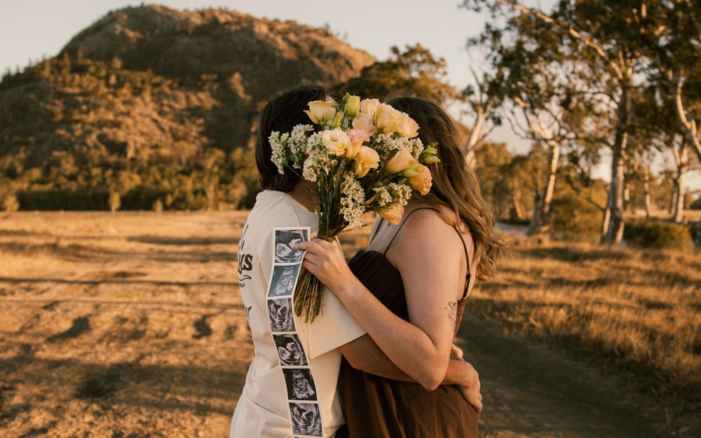 Two people sharing a romantic embrace with a bouquet of white flowers in a golden field with a mountain backdrop. Rockhampton Queensland