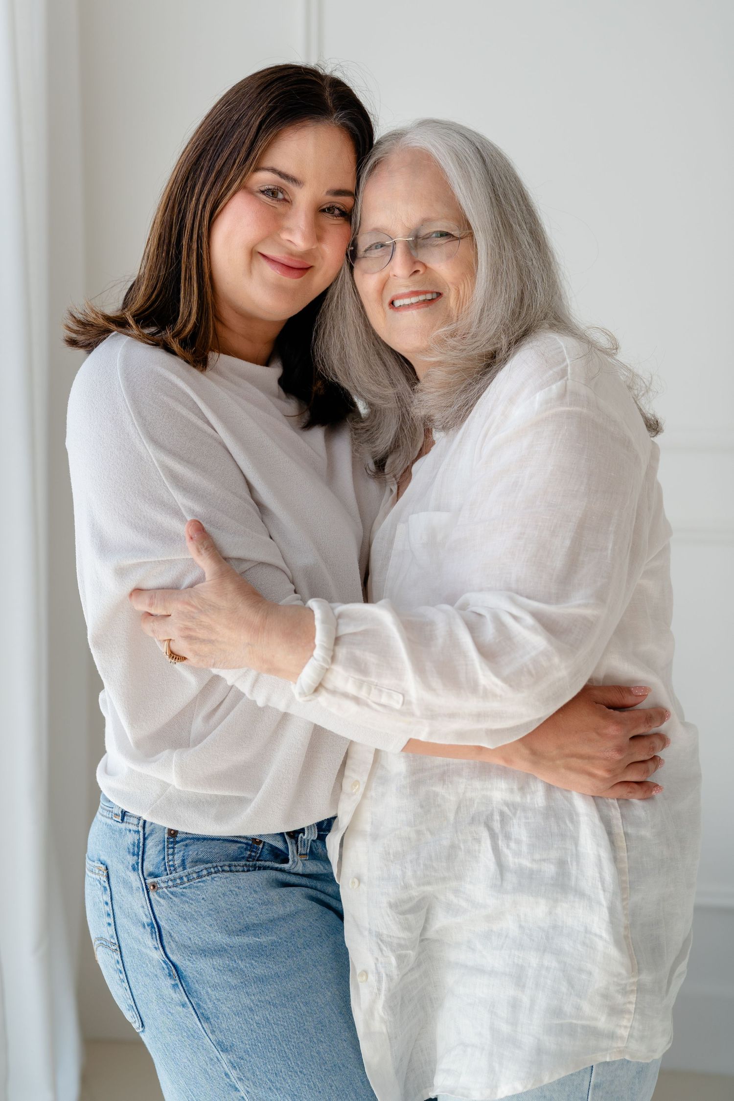 Multi-generational family portrait with grandmother, two teen girls, and two young children posing together on a white bed.
