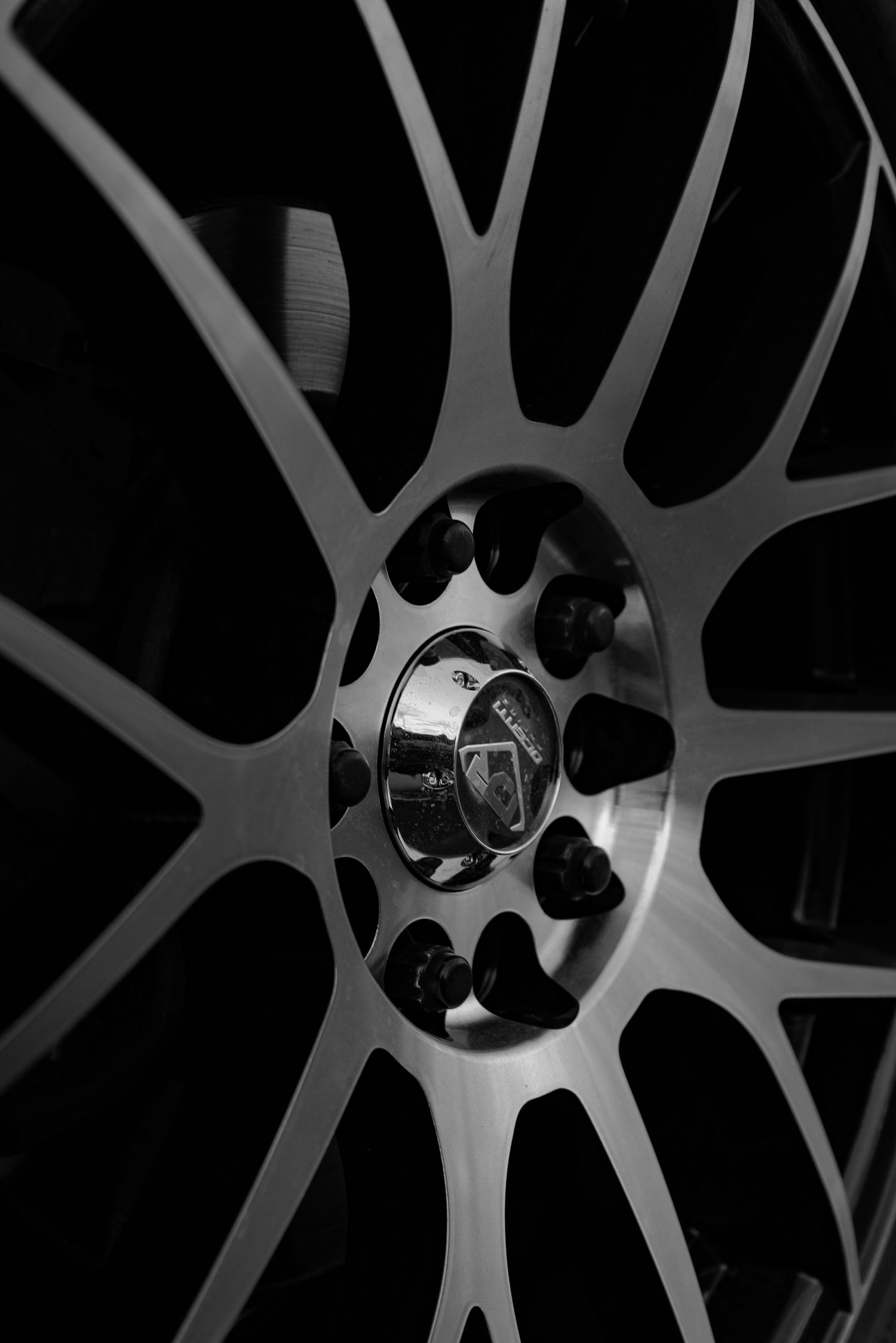 Close-up black and white detail of a luxury car wheel rim showing intricate spoke design and Mercedes-Benz center cap.