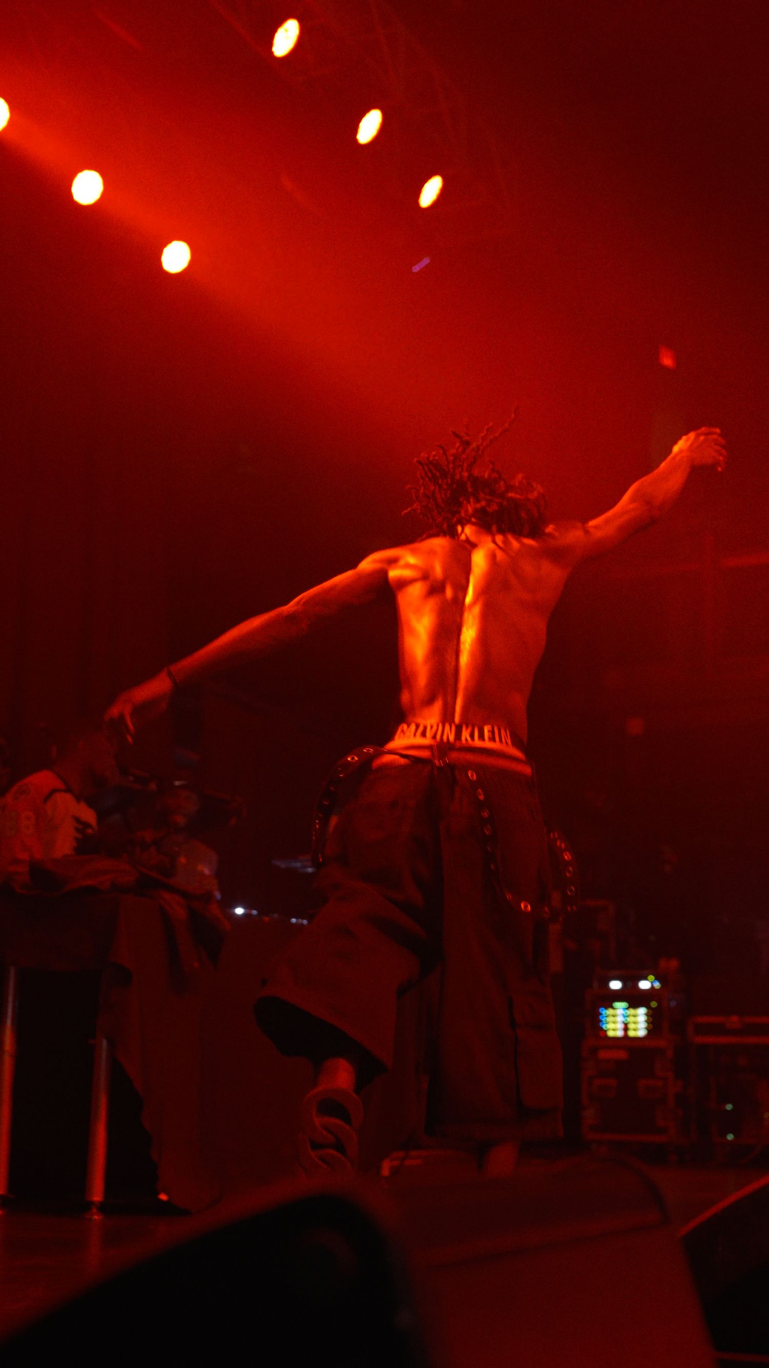 Silhouetted performers on stage with dramatic red lighting.