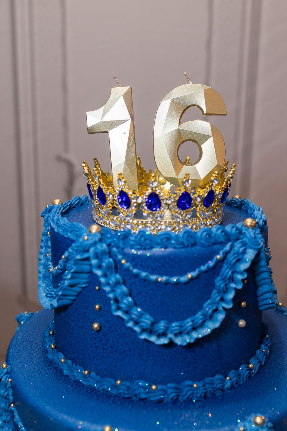 Blue and gold Sweet 16 birthday cake with crown topper and number 16 candles.