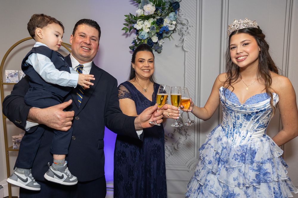 Family celebrating a quinceañera, toasting champagne with a girl in a blue floral gown and tiara at an elegant party.