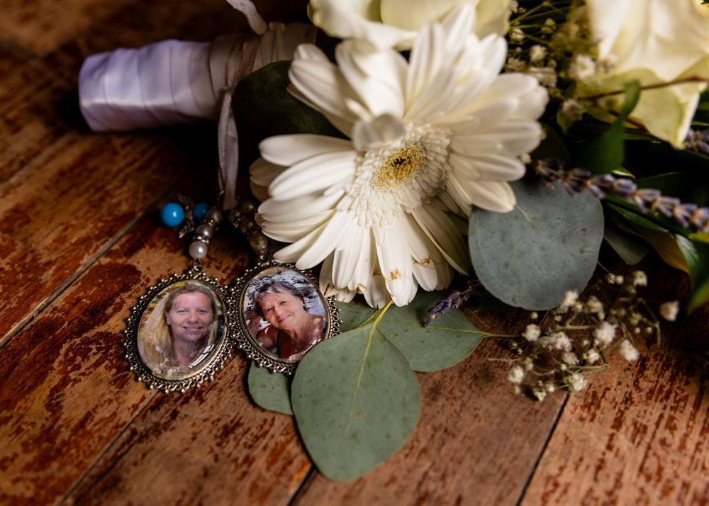 Wedding bouquet with white daisies and memorial photo charms on wooden surface.